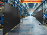 Industrial factory floor with rows of black wheeled divider panels lining a wide production aisle.