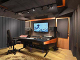 Professional audio mixing studio with a control desk, speakers, monitor screen, and acoustic wall panels.