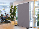 Freestanding gray divider panel in a modern office lounge near glass doors and seating.