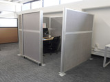 Gray fabric office cubicle with a frosted sliding door opening to a small desk workspace