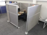 Person working at a desk inside gray fabric office cubicle panels with a frosted sliding partition.