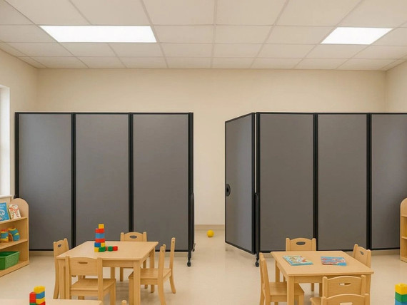 Preschool classroom with small tables and chairs, divided by two gray wheeled partition panels.