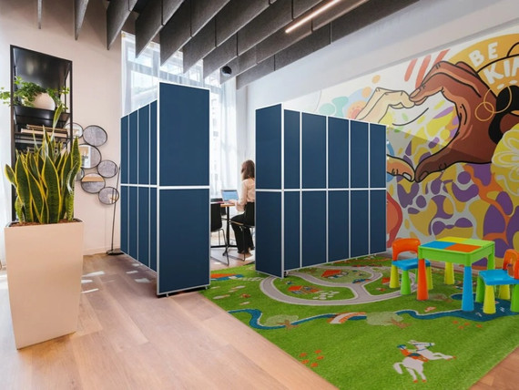 A modern, colorful indoor space with blue partition panels creating a semi-private work area where a person sits at a laptop.