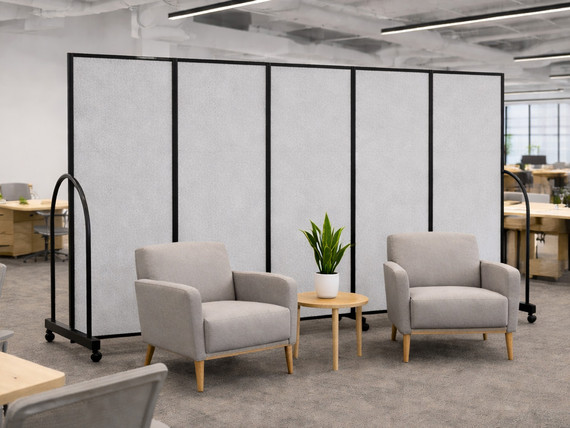 Two lounge chairs and a small table with a plant set in front of a gray rolling partition wall in a modern office.