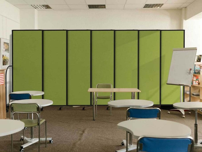 Green modular partition panels forming a backdrop in a classroom with study tables, chairs, and a whiteboard.
