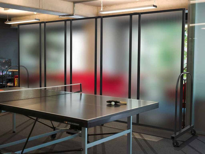Ping‑pong table set in front of tall frosted rolling partition panels in a modern office recreation area.