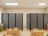 Preschool classroom with small tables and chairs, divided by two gray wheeled partition panels.