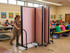 Mobile pink fabric room divider being rolled through a school cafeteria with children seated at tables.