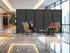 Two people seated in a modern lobby, partially screened by a large black wheeled divider panel.