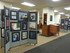 Library interior with wheeled divider panels displaying framed artwork, arranged as a gallery exhibit.