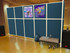 Blue freestanding partition wall with posters in a dance studio, with a bench, shoes, and a backpack on a wooden floor.