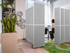 Gray freestanding partition panels forming a small workspace, with a person using a laptop beside indoor plants.