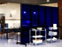 Restaurant interior with blue translucent partition panels on wheels, separating dining tables from serving carts stacked with plates.