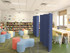 Library reading area with colorful seating and tables, divided by tall blue freestanding partition panels.