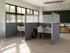 Office workstations created with fabric and frosted partition panels, featuring desks, chairs, and backpacks near large windows.
