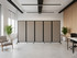 Modern office space with a row of beige fabric privacy screens on wheels, flanked by chairs and potted plants.
