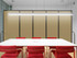 Conference room with a long white table and red chairs, set against beige acoustic wall panels under a linear pendant light.