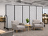 Two lounge chairs and a small table with a plant set in front of a gray rolling partition wall in a modern office.