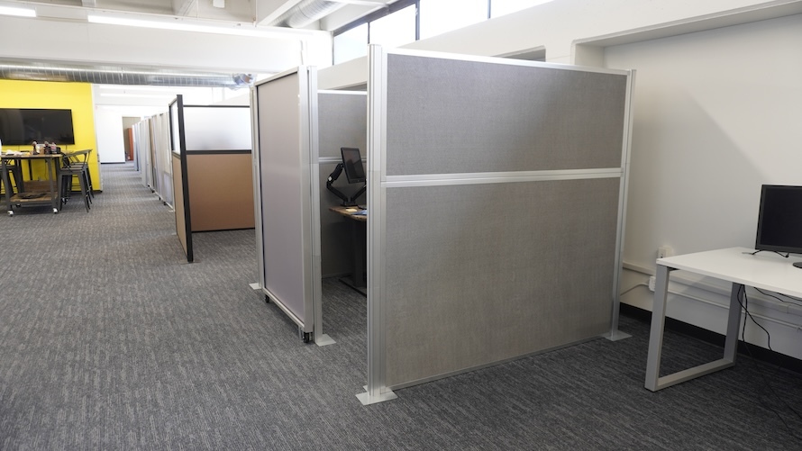 Row of partitioned cubicles in an open-plan office with carpeted floors and desks.