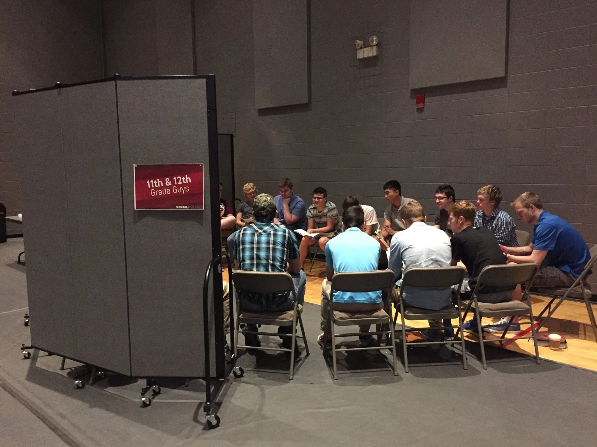 Black room divider creates privacy for high school boys' small group meeting Grey room divider creates privacy for a youth's small group gathering in a gym