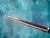 Full spliced purpleheart Giuli Sneaky Pete pool cue with Keilwood shaft laid on teal textured background