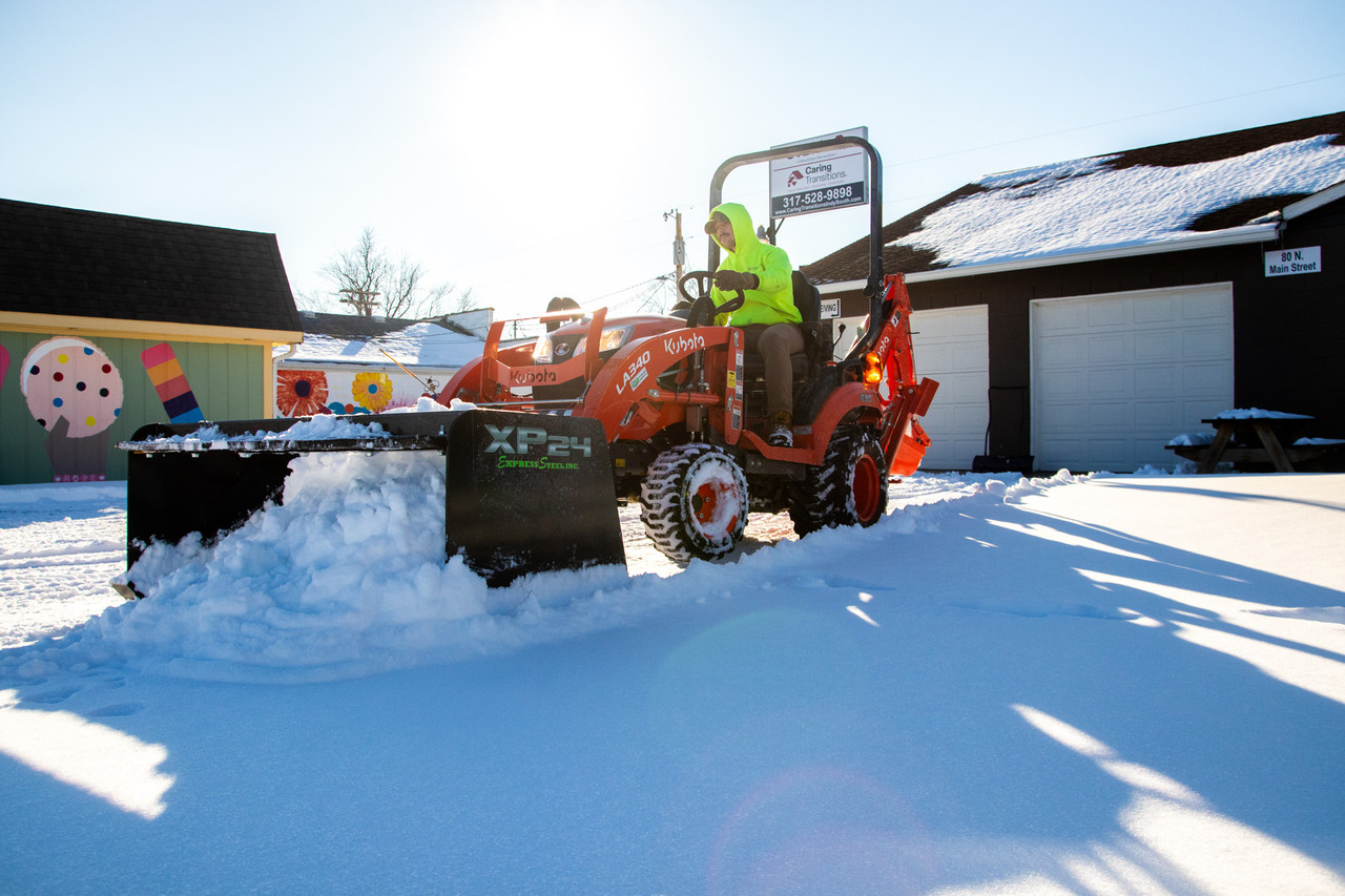 Operator clearing a snowy lot with an Express Steel XP24 pusher on a compact tractor