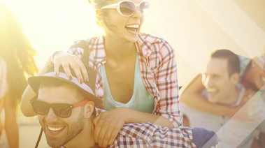 A woman is sitting on a man's shoulders, smiling and cheering, surrounded by a group of friends who are laughing and having a great time.