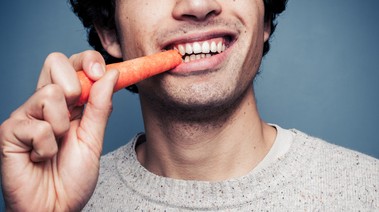A person taking a bite of a carrot.