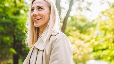 Smiling blonde woman standing outside looks happily to the side.