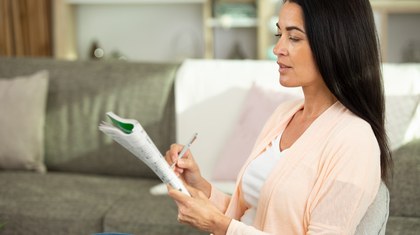Woman sitting on a couch focuses on solving a crossword puzzle.