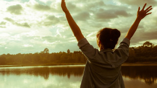 A lady raising both the hand near the lake.