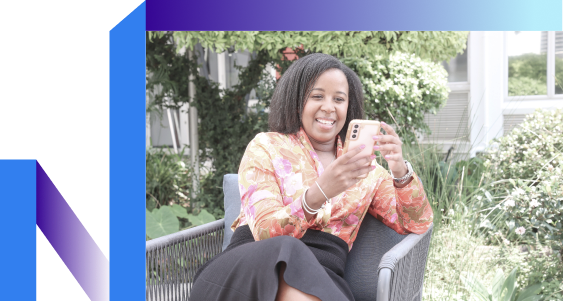 A woman sitting on chair looking at mobile with a smile on her face.