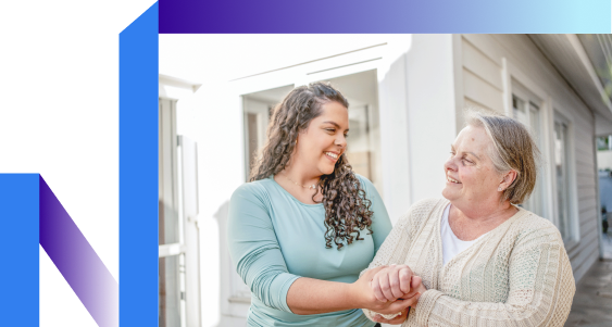 A woman and an older woman hold hands outside, symbolizing connection in a sunny setting