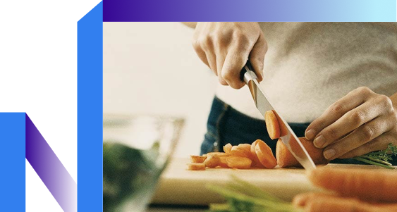 A close-up of a person chopping vibrant orange carrots on a cutting board.