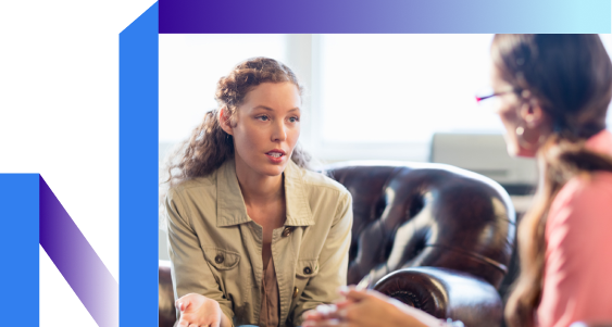 Two women on a couch share smiles and ideas in conversation.