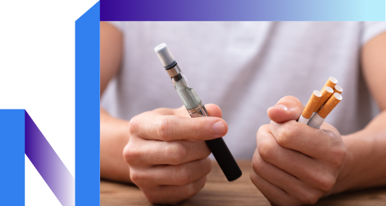 A person holds a vape pen in one hand and several cigarettes in the other, sitting at a table.