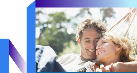 A couple smiling and relaxing together in a hammock under a sunny sky with trees in the background.