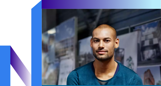 A person with a shaved head, wearing a blue shirt, is sitting indoors.