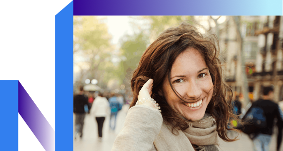 A smiling woman with wavy brown hair stands on a busy street, wearing a scarf.