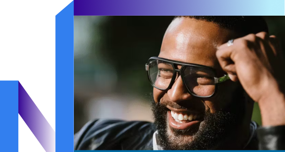 A warm, smiling man with glasses and a beard in a casual setting.