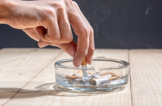 A hand with a cigarette over a glass ashtray, symbolizing tobacco's lingering effects.