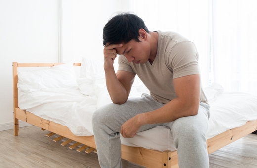 A man sits on a bed, head in hands, pondering how smoking less can improve his sleep.