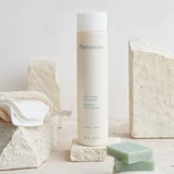 Invigorating Cleansing Lotion Face and Eyes, 250 ml bottle sitting on a table next to sandstone and bars of soap.