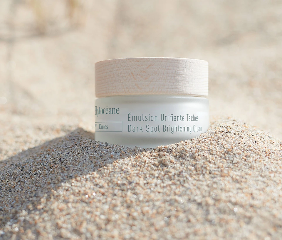 Phytoceane Dark Spot Brightening Cream with Organic Sand Lily, 50 ml jar on a pile of sand.