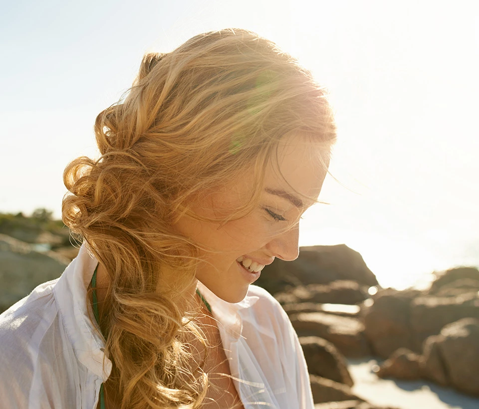 Woman gazing down, smiling, while on the beach.