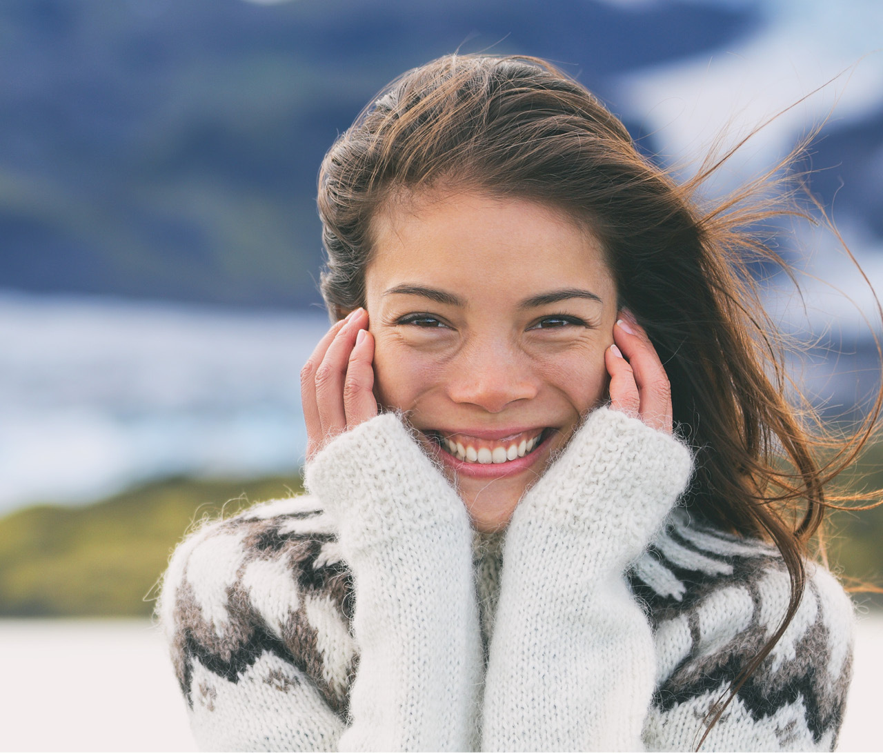 A woman smiling into the camera wearing a thick wool sweater.