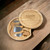 A round wooden cheese board engraved with the word ‘Daddy’ on the lid, shown slid open to reveal a hidden compartment holding four stainless steel cheese servers neatly fitted into slots inside the board