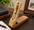 A light-coloured wooden pen case that functions as a display stand, holding a two-tone wooden  pen. The base is engraved with the text: Alex Webster, Congratulations on your Graduation, Leicester University 2023, Love Mum & Dad.