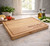 Hand chopping vegetables on large personalised wooden butcher block board in modern kitchen, centered engraving visible