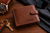 A brown leather wallet with the name "A.J. COLE" and a Visconti logo embossed on the front. A gold watch, sunglasses, and keys are also visible on a wooden surface.